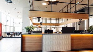 A modern reception area with a wooden reception desk, multiple pendant lights, and a large window providing natural light. - harry’s home Steyr hotel & apartments (Steyr)