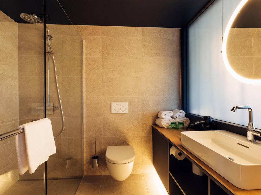 Un baño moderno con cabina de ducha de vidrio, un inodoro, un lavabo con espejo y un perchero para toallas.