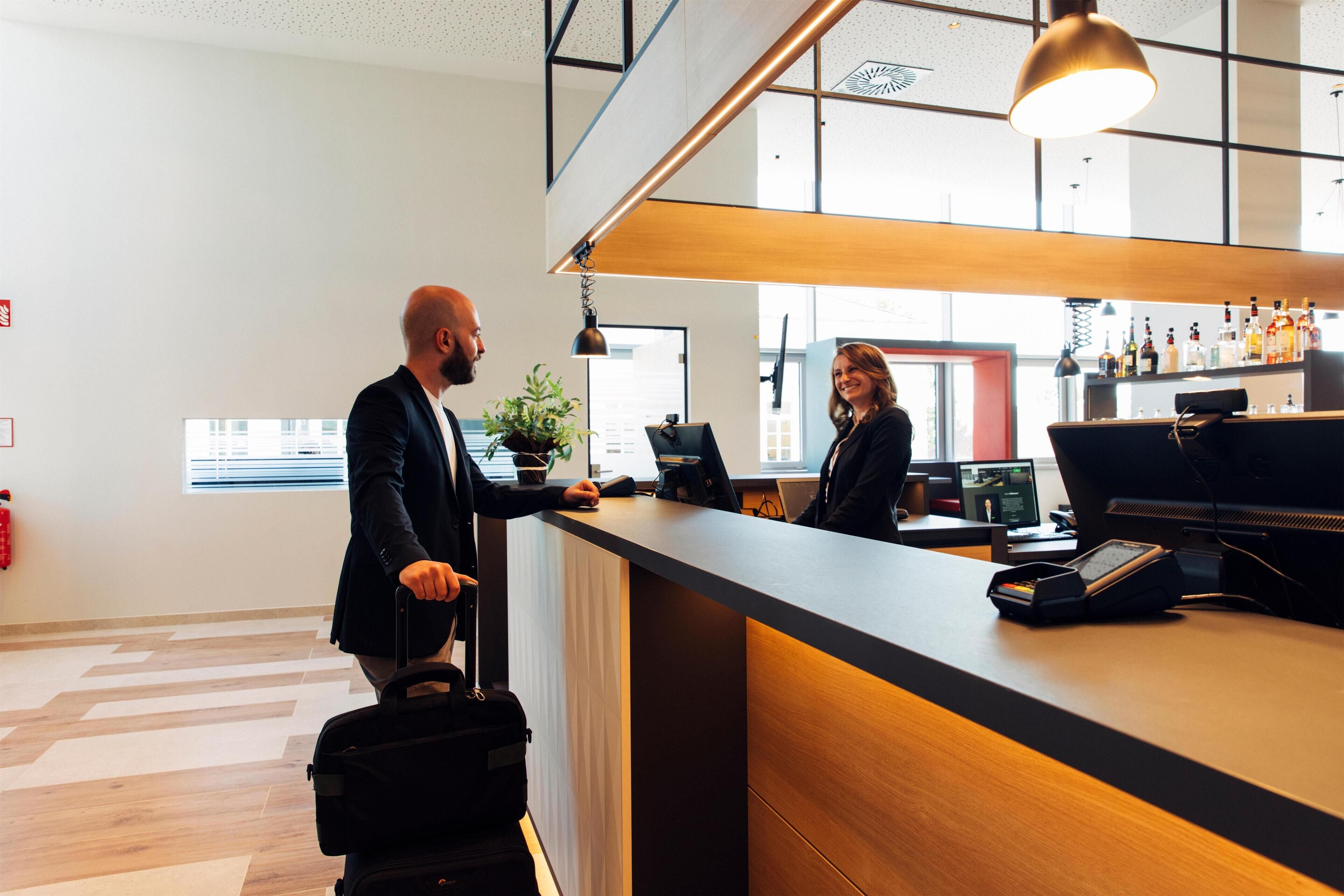 Een moderne hotel receptie met een houten balie, een computer en een plant.