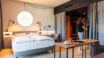 A modern hotel room with a neatly made bed, bedside lamps, a table with a cup and a plate, and a wardrobe.