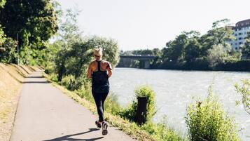 A person jogging on a paved path beside a river, with trees and a bridge in the background.