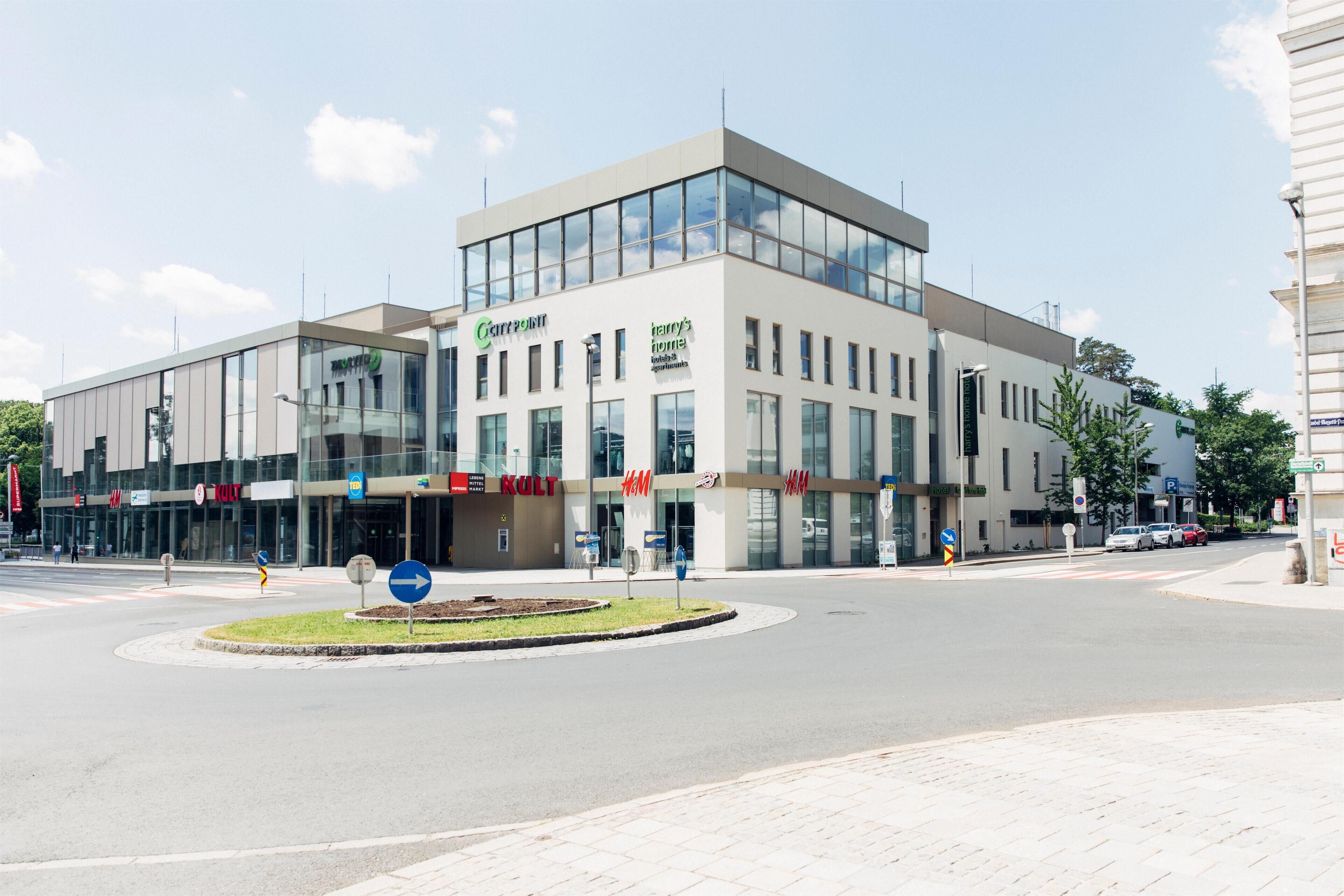 A modern building with large glass windows and multiple commercial signs, including 'Cartridge' and 'KULT'.