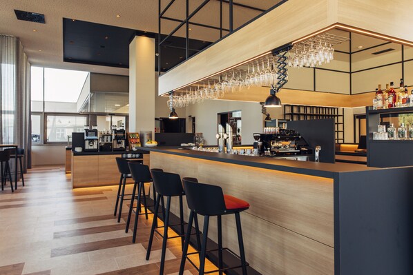 Een moderne bar met een lange toonbank, meerdere barkrukken en een divers aanbod aan flessen en glazen.