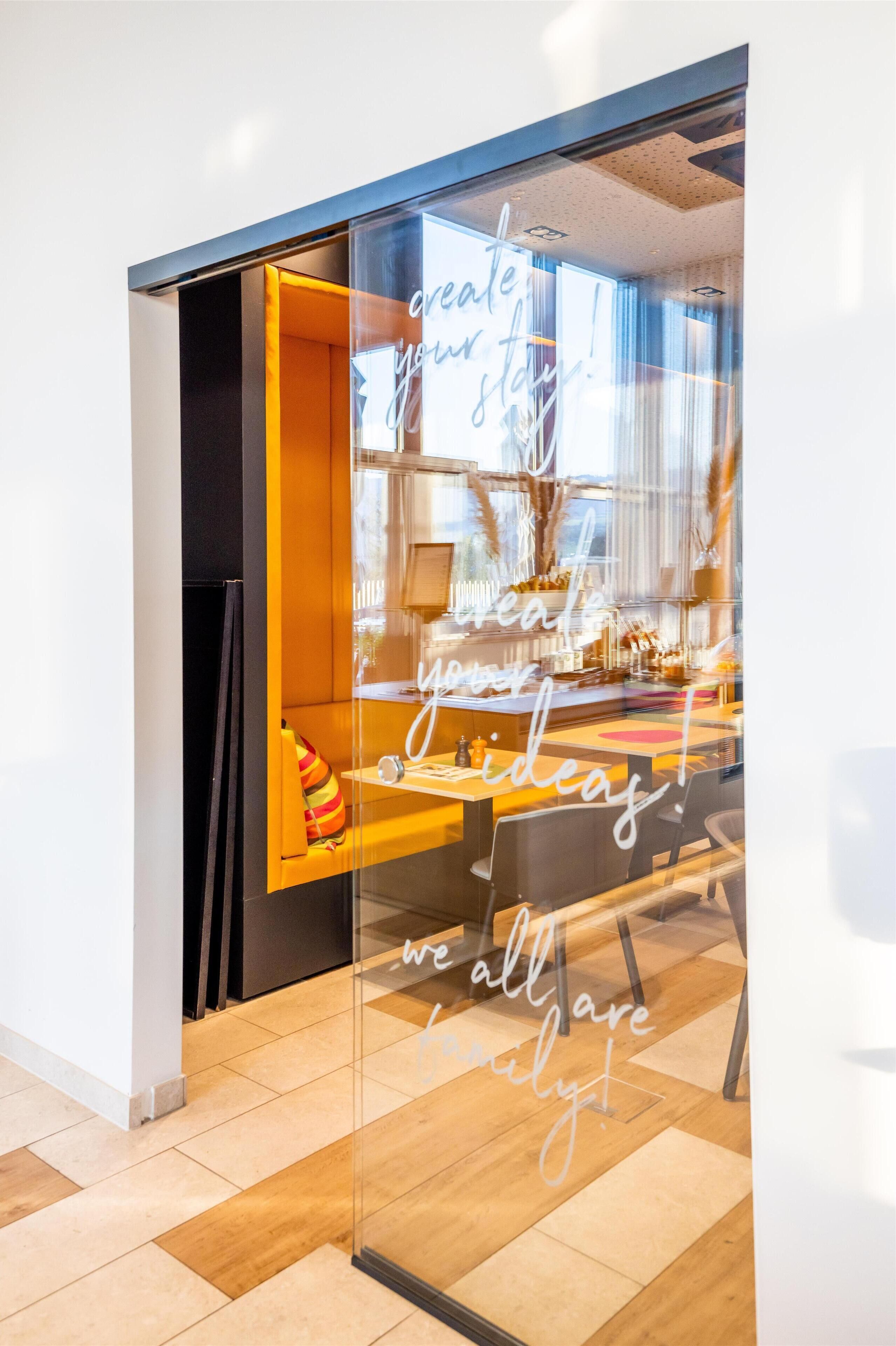 A modern interior with a glass partition displaying motivational text, a wooden bench, and a well-lit workspace.