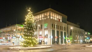 A modern hotel with a Christmas tree in front, large windows, and a parking area. - harry’s home Steyr hotel & apartments (Steyr)