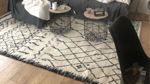 Un salon chaleureux avec un canapé gris, deux petites tables rondes, un tapis à motifs et une plante en pot.
