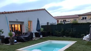 Un jardin avec une piscine rectangulaire, un espace salon couvert et une pelouse.
