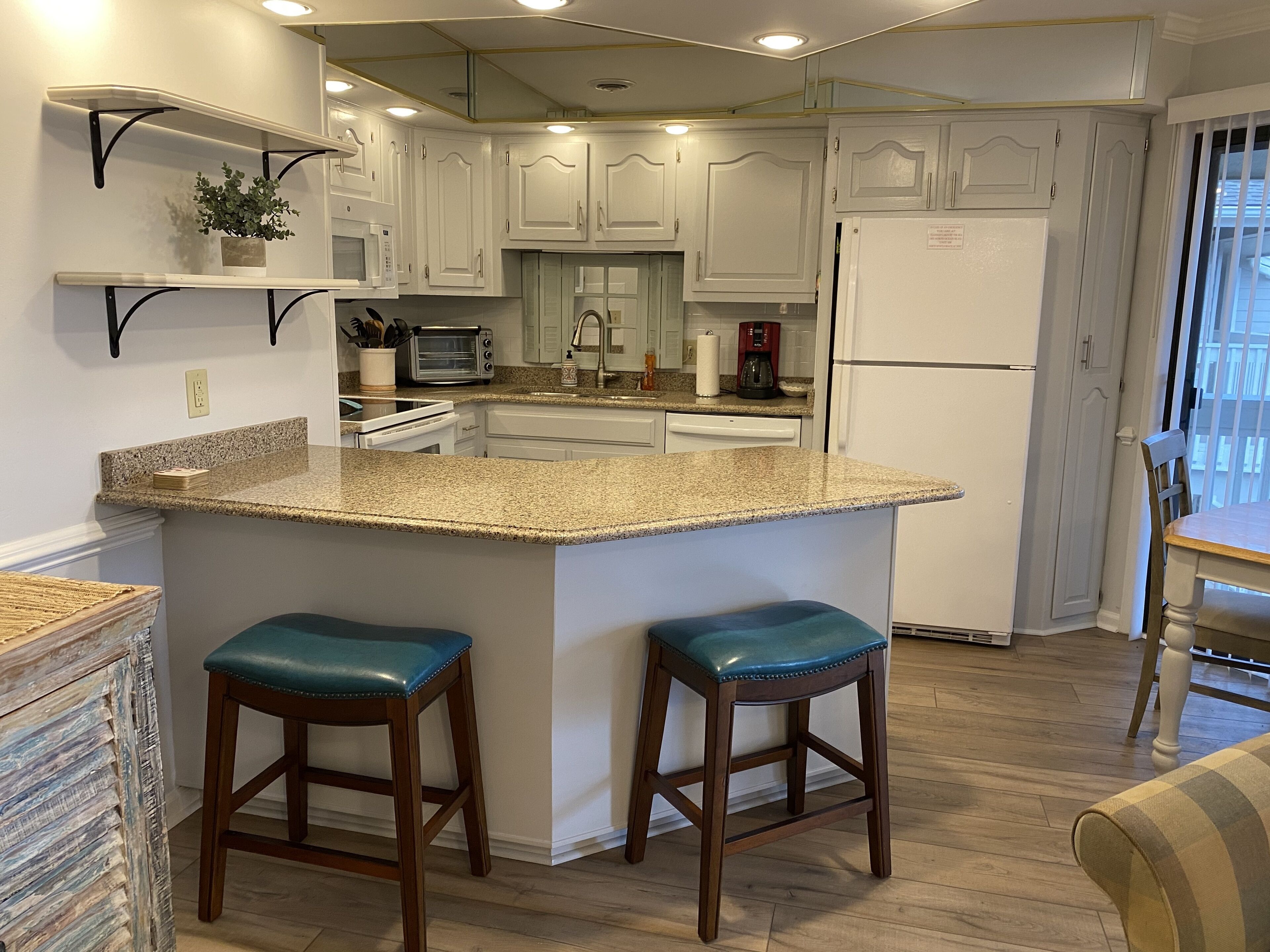 A kitchen with white cabinets, a granite countertop, two bar stools, a microwave, a toaster, and a refrigerator.