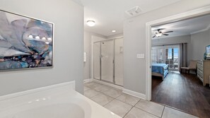 A modern bathroom with a bathtub, a glass shower enclosure, and a large abstract painting on the wall.