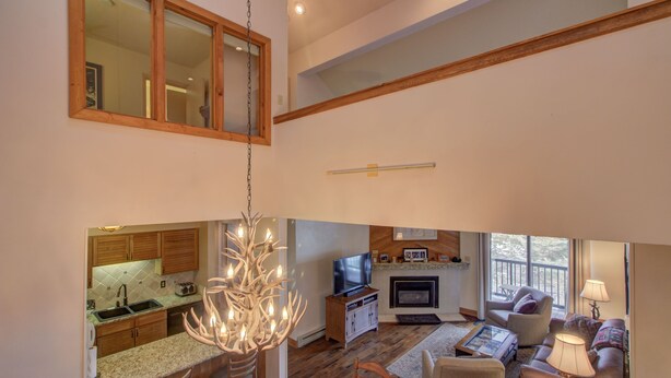 A spacious living area with a kitchen, dining table, and seating. A television and fireplace are visible. - Spacious 3-Bedroom + Loft Condo at Timber Run – Sleeps 10, Walk to Slopes! (Steamboat Springs)
