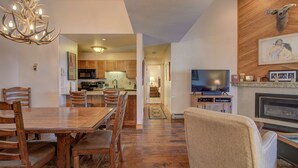 A spacious living room with a fireplace, a television, and a dining area with wooden furniture. - Spacious 3-Bedroom + Loft Condo at Timber Run – Sleeps 10, Walk to Slopes! (Steamboat Springs)