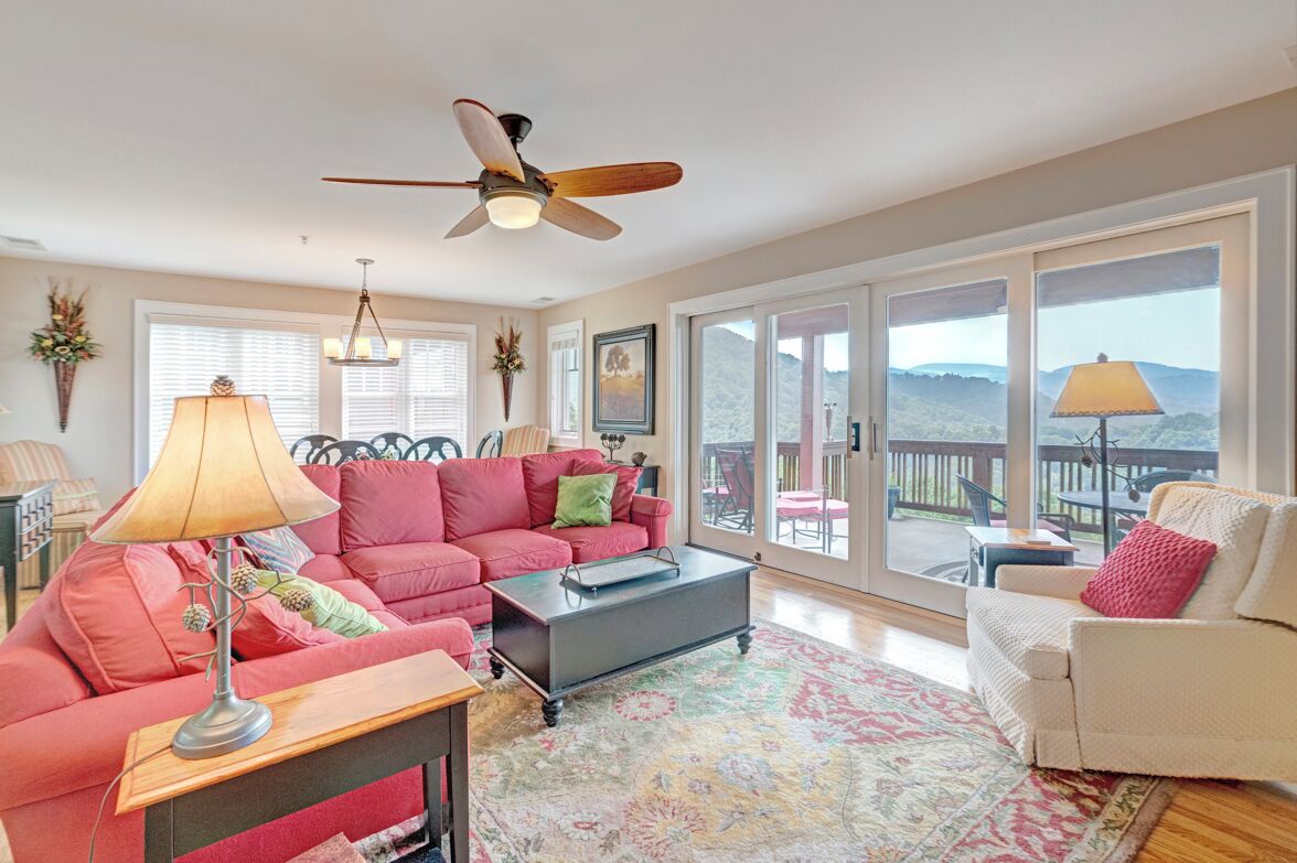 A spacious living room with a large window, a ceiling fan, and a cozy seating area.