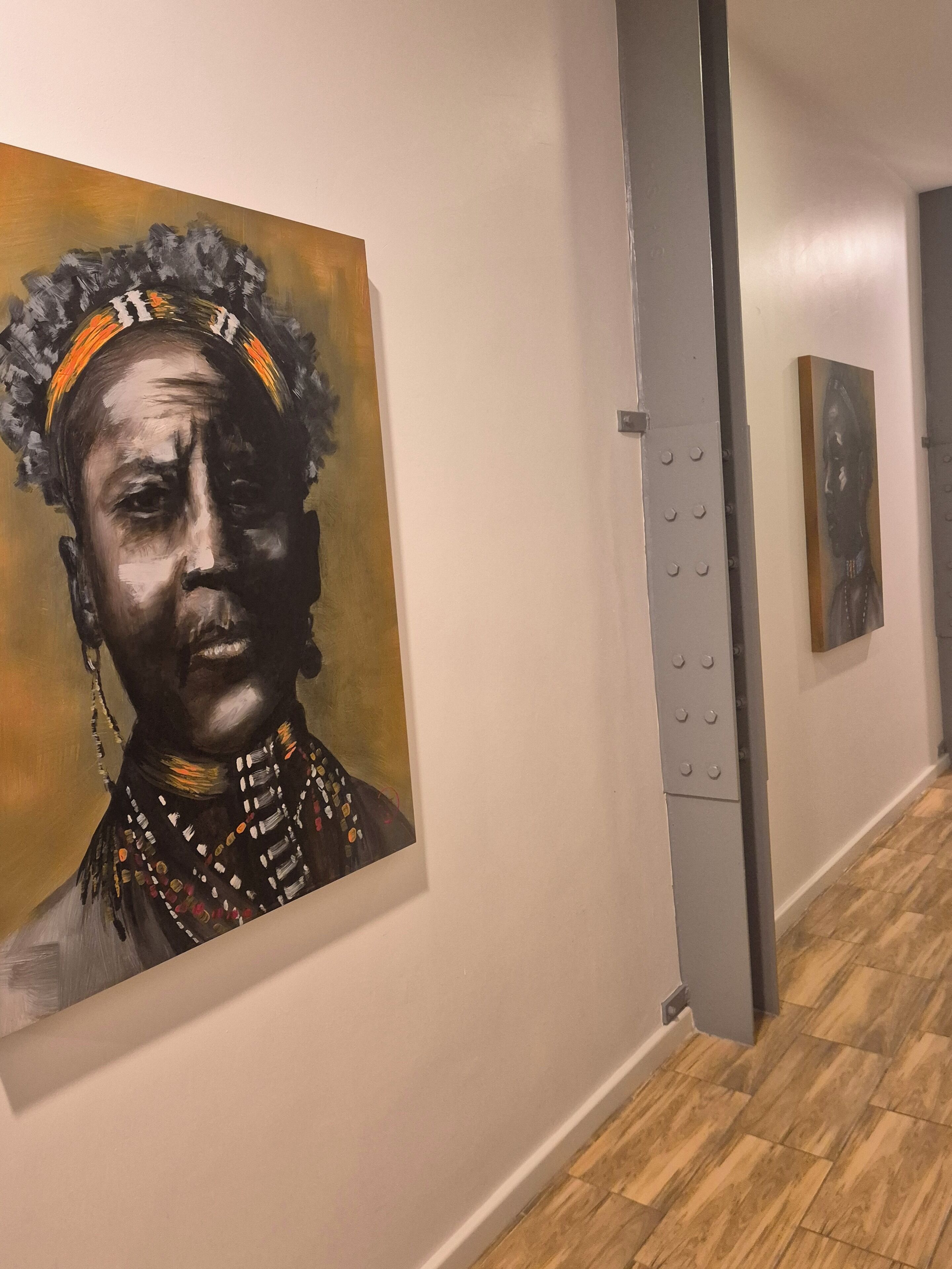A hallway with artworks on the walls, a wooden floor, and a grey structural element.