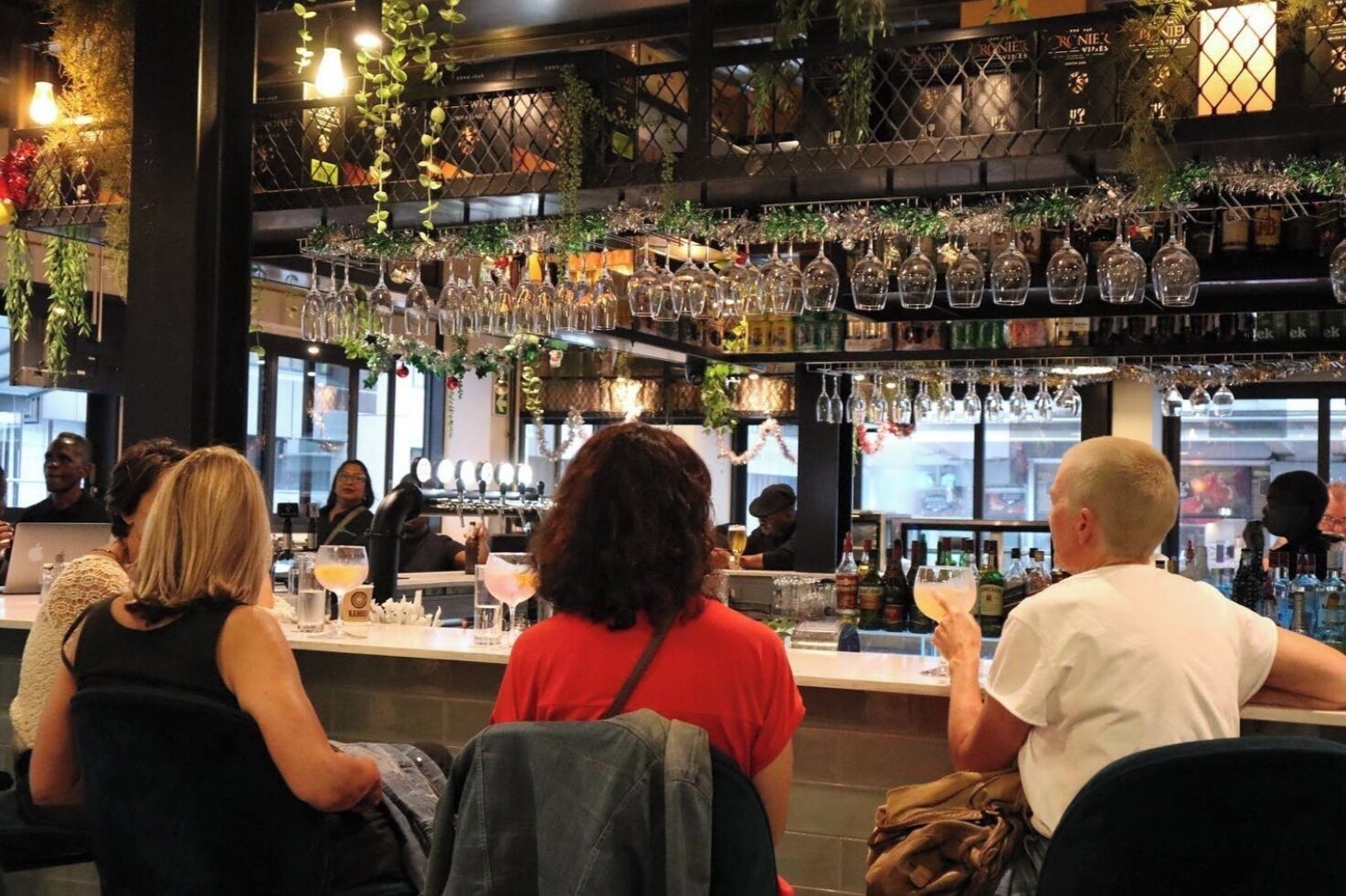 A bar area with multiple patrons seated, a bartender at the counter, and a variety of bottles and glasses on shelves.