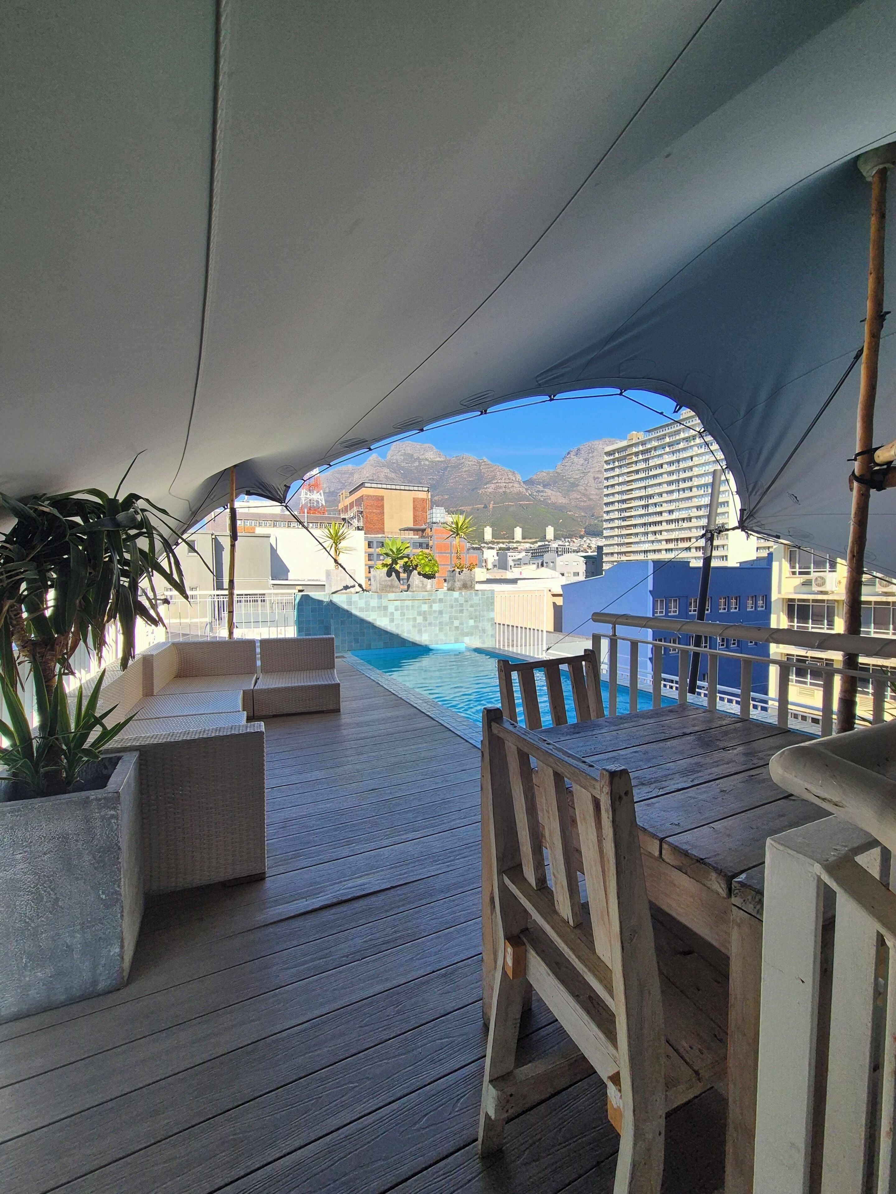 A wooden deck with a pool, outdoor seating, and a view of buildings and mountains.