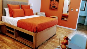 Una habitación de hotel moderna con una cama de madera, ropa de cama naranja, un espejo grande y vistas al pasillo.