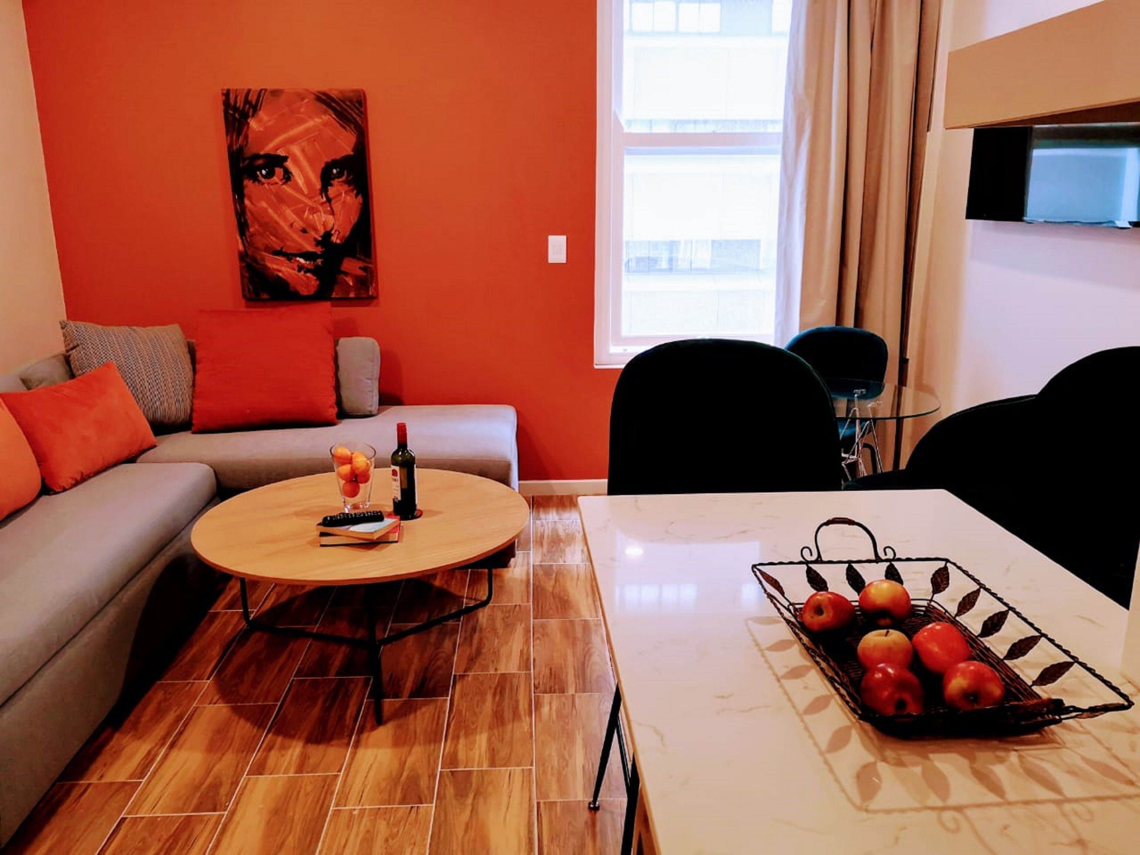 A living room with a sofa, a coffee table, a dining table with a fruit basket, and a painting on the wall.