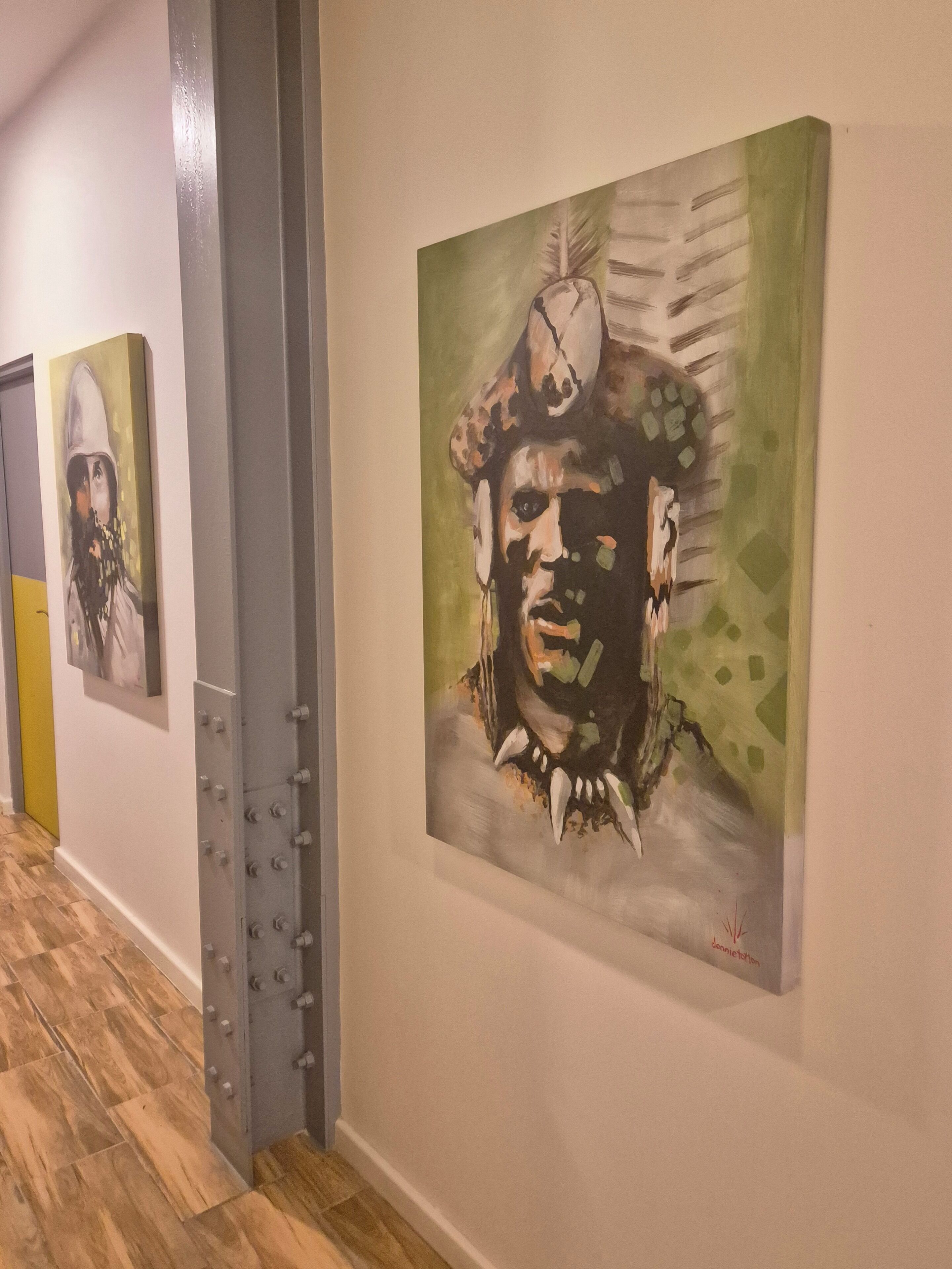 A hallway with artworks on the walls and a metallic structure on the left.