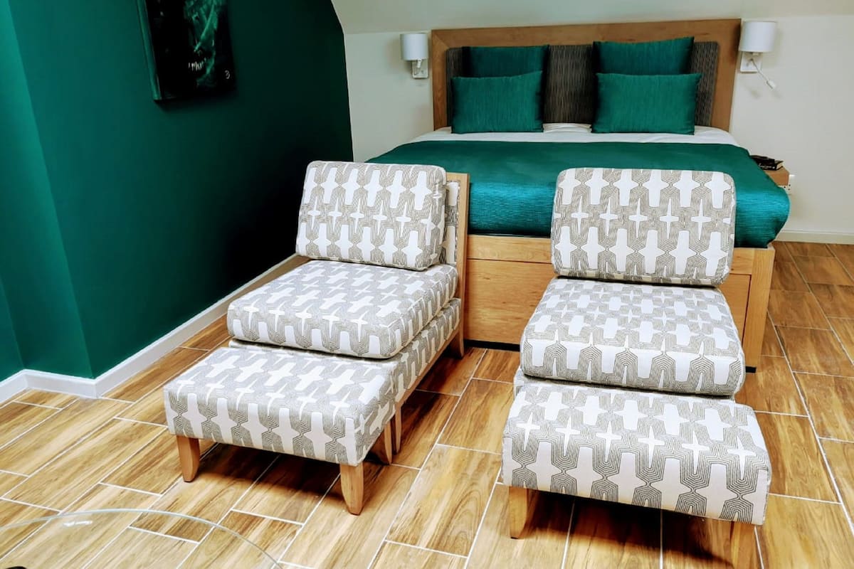 Un dormitorio con una cama, dos sillones a juego, una mesita de noche de madera y una pared de acento verde.