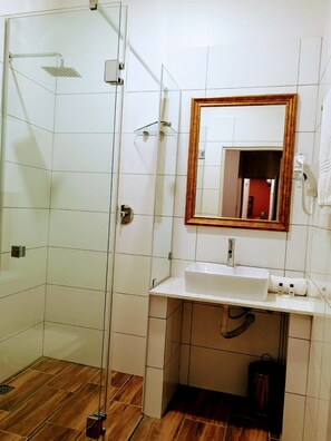 Bathroom features a glass-enclosed shower with handheld showerhead and wall-mounted controls, a sink with a mirror, and a tiled floor.