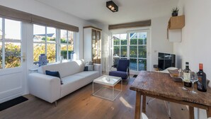 Una sala moderna con un sofá blanco, una mesa de centro y una mesa de comedor con acabado rústico. Hay un televisor y una botella de vino sobre la mesa.