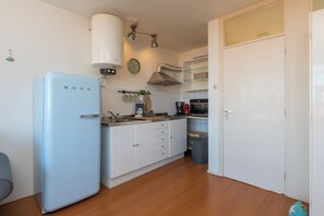 A compact kitchen with a blue refrigerator, white cabinets, a sink, a stove, and a microwave.