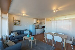 A compact living space with a sofa, a dining table with chairs, a kitchenette, and a wardrobe.