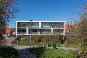A modern two-story building with balconies, a paved pathway, and surrounding greenery. - Apartment - Duinstraatje 21 | Zoutelande (Zoutelande)