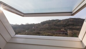 A skylight window with a view of a hilly landscape and a small building. - Apt - Duinweg 117-4 | Zoutelande 'Duinoo (Zoutelande)