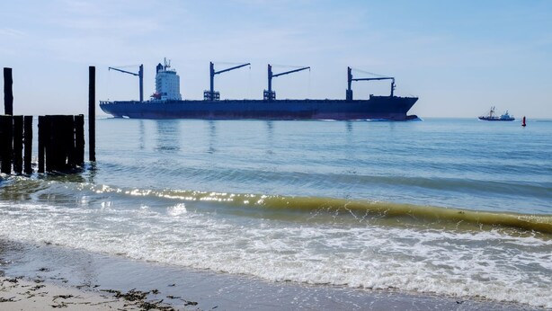 A large cargo ship docked at a pier with a smaller vessel in the background.