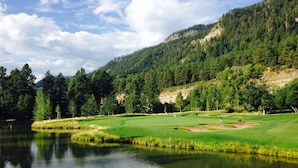 Un camp de golf tranquil amb un llac, envoltat per un bosc dens i turons.