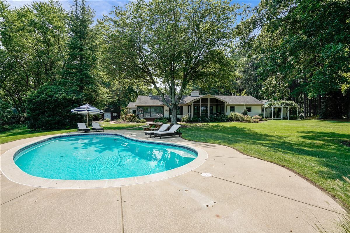 A backyard with a swimming pool, two lounge chairs, and a covered patio area.