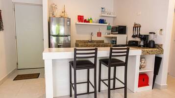 A compact kitchen with a refrigerator, microwave, coffee maker, and a small island with two chairs.