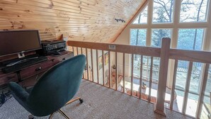 Una habitación con techo inclinado, paredes de madera, un escritorio con computadora y vistas amplias a través de grandes ventanales.