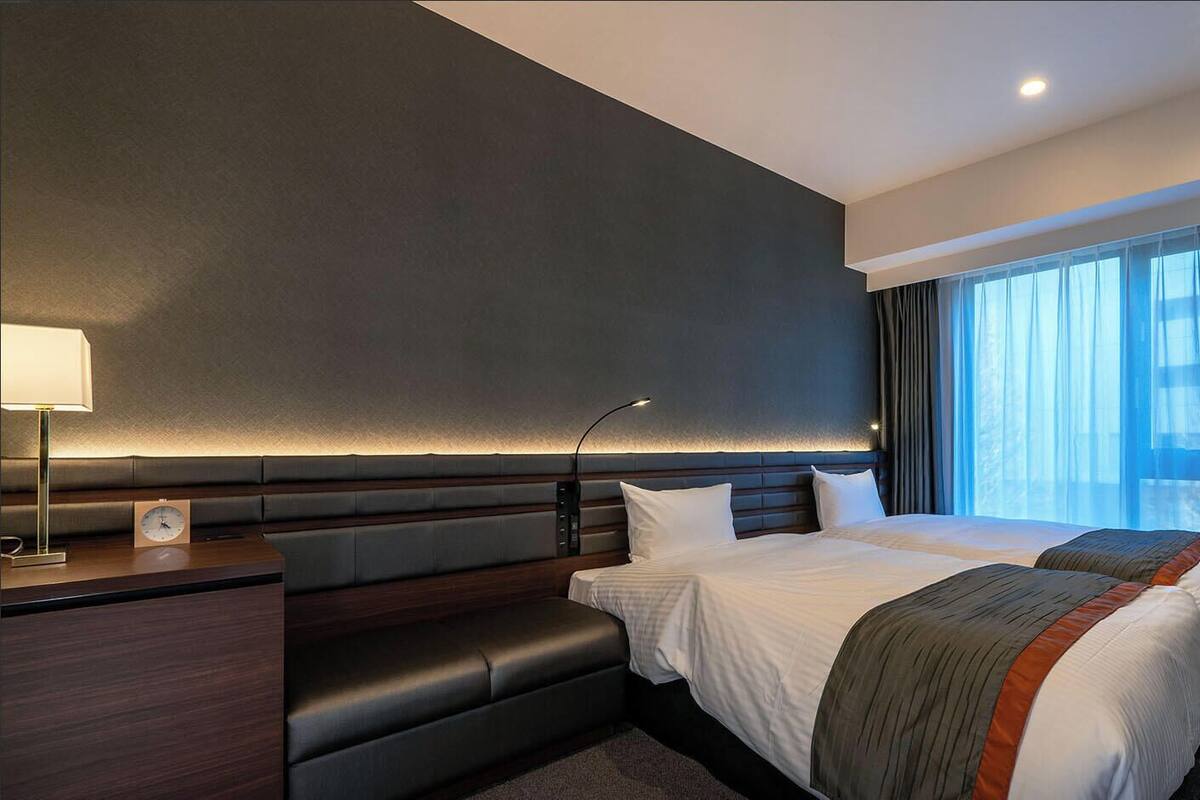 Una habitación de hotel moderna con una cama grande, un escritorio, una silla y una ventana con cortinas.