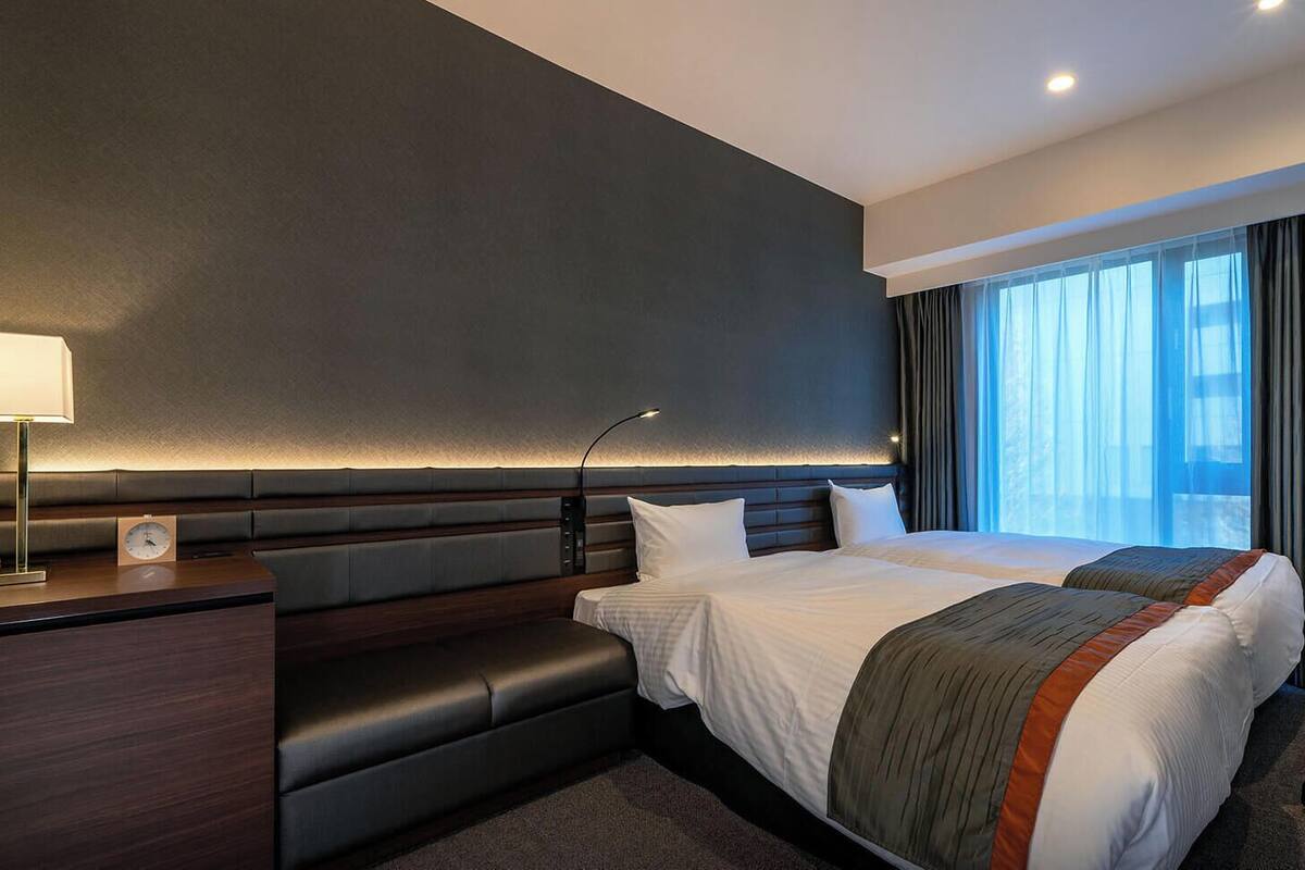 Una habitación de hotel moderna con una cama grande, un escritorio, una silla, un televisor y una ventana con cortinas.