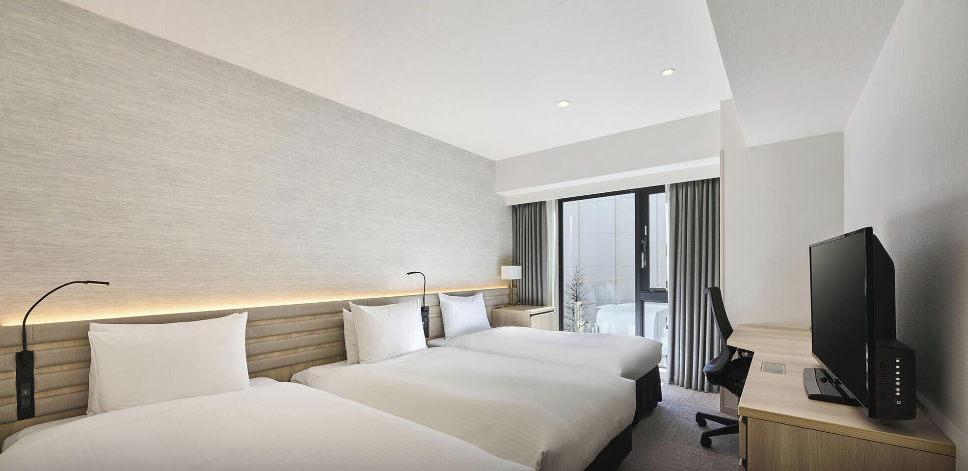 A hotel room with two beds, a TV, a desk, and a window with curtains.