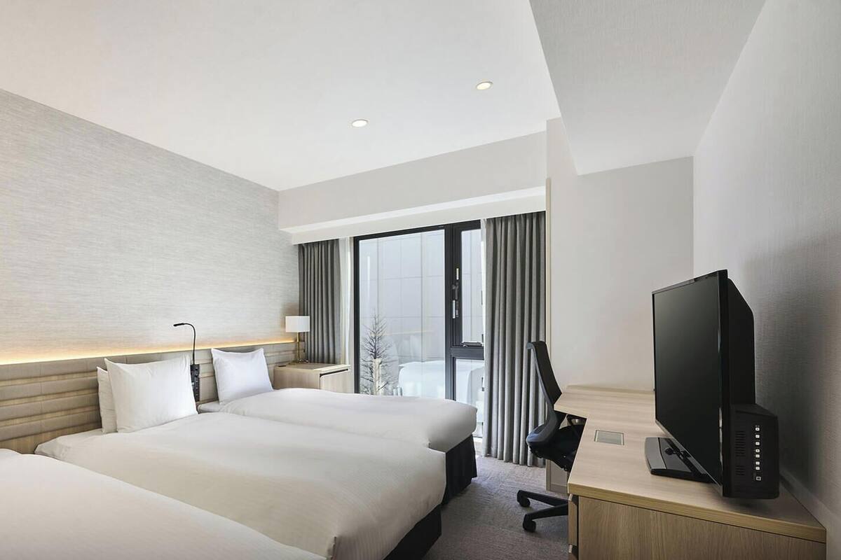 Habitación de hotel con dos camas, televisión, escritorio y ventana con cortinas.