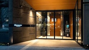 A modern hotel entrance with a wooden overhang, glass doors, and a sign indicating a "Business Center."