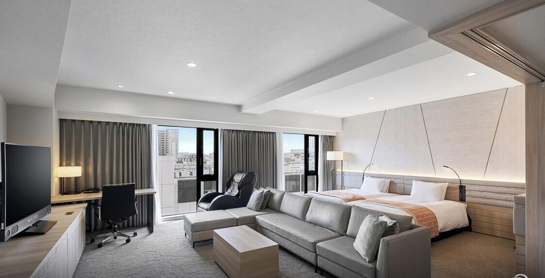 A modern hotel room with a large bed, a sofa, a desk, and a TV.