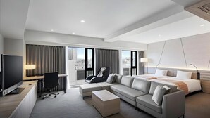 A modern hotel room with a sofa, a desk, a chair, a bed, and a TV.