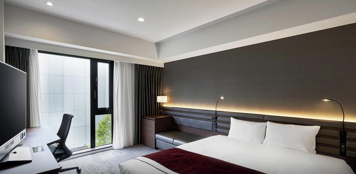 A modern hotel room with a large bed, a desk with a chair, a TV, and a view of the outdoors.