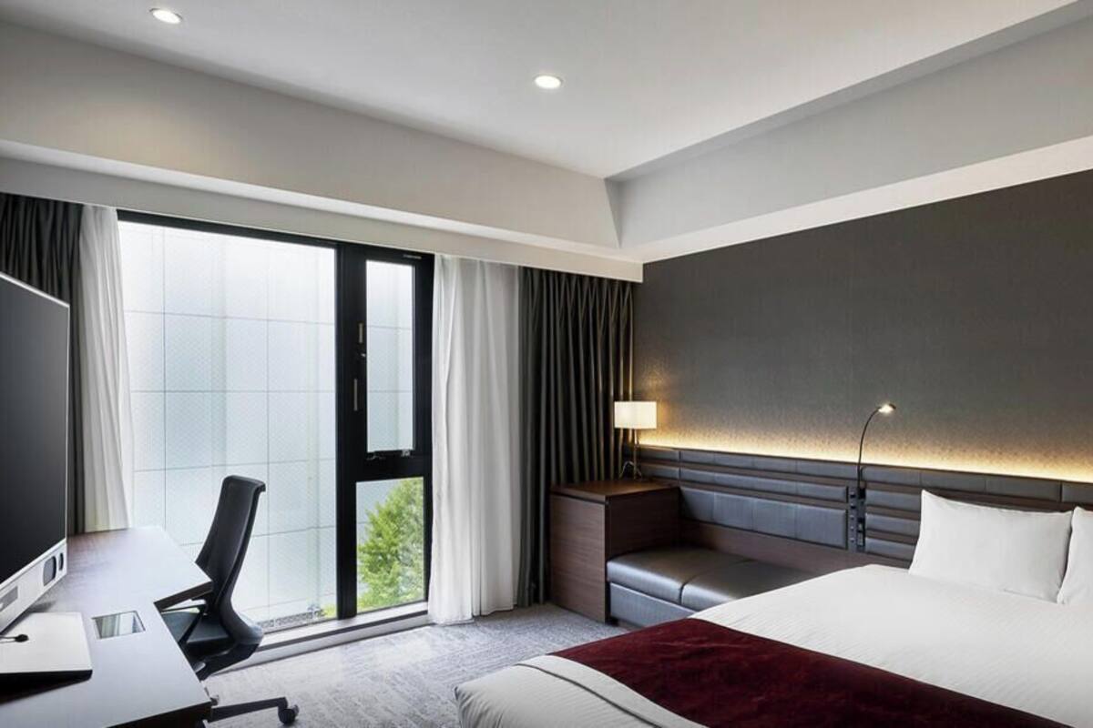 Habitación de hotel moderna con una cama grande, un escritorio con silla, un televisor y vistas al exterior.