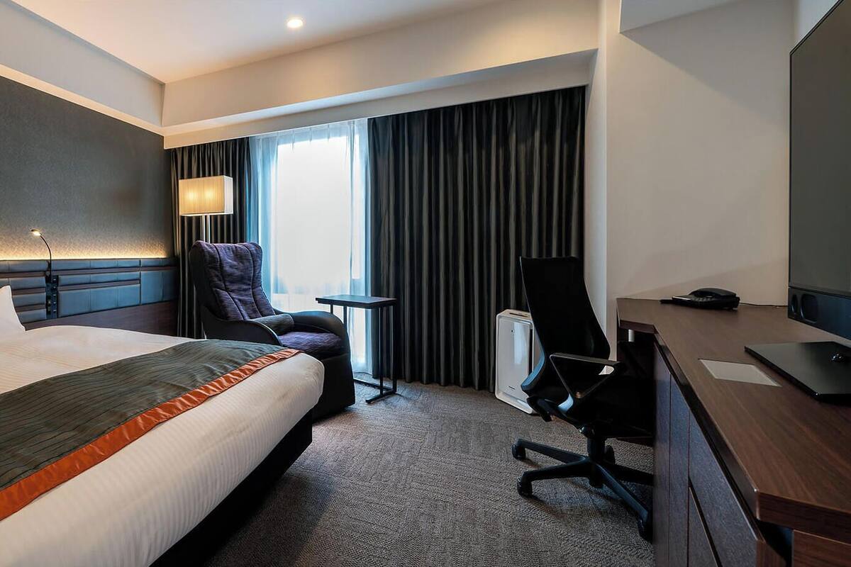 Una habitación de hotel con una cama grande, un escritorio, una silla, una lámpara y un televisor.