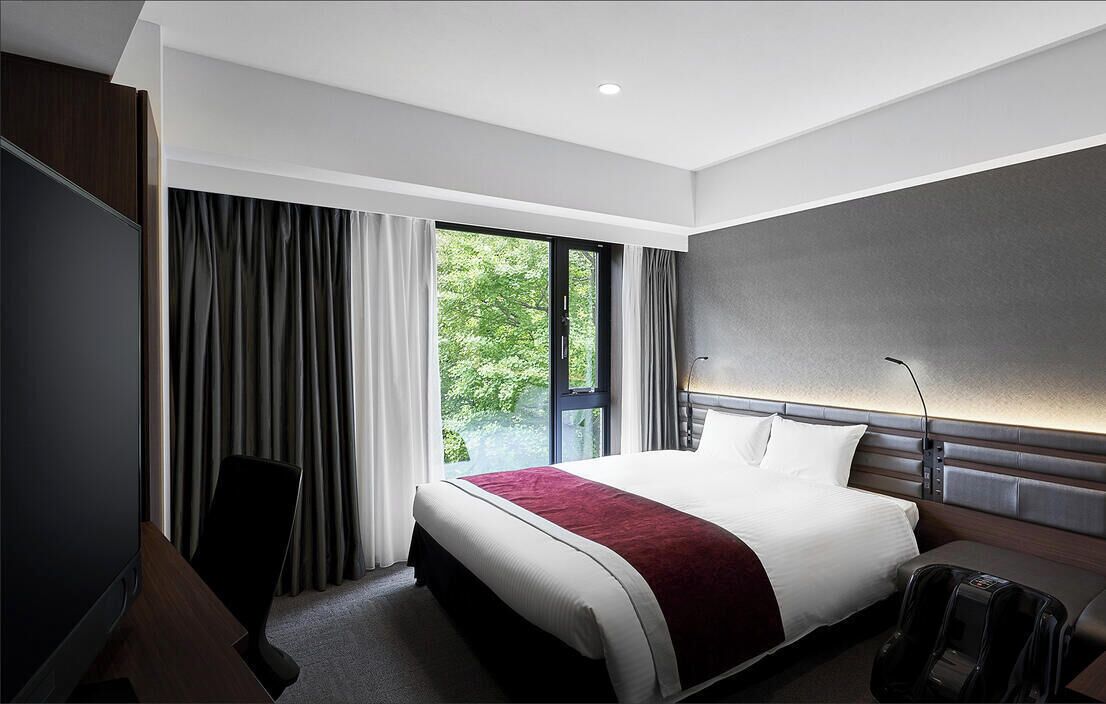 A modern hotel room with a large bed, a desk, and a massage chair.