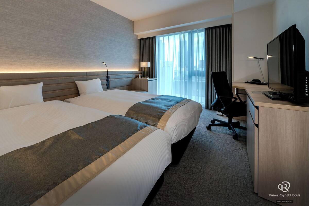 Una habitación de hotel con dos camas, un escritorio con computadora y televisión.