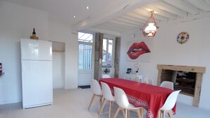 Uma sala de jantar com uma mesa e cadeiras brancas, um refrigerador branco e uma lareira.