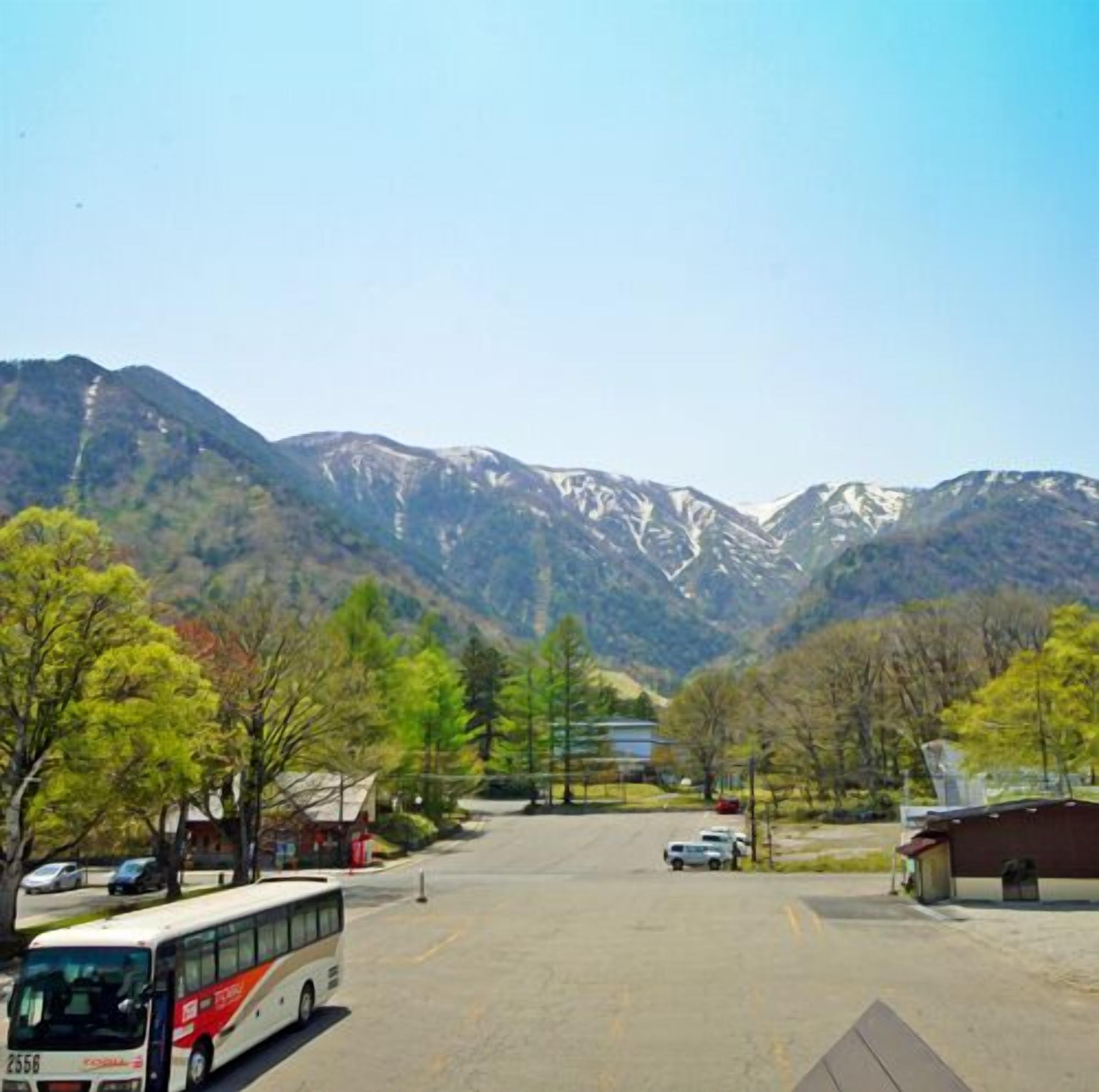 A parking lot with a bus, trees, and mountains in the background.