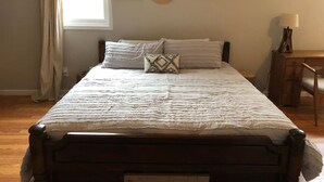 A bedroom with a wooden bed, white bedding, a desk, and a lamp.