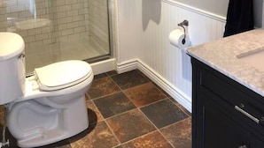 A bathroom with a glass shower enclosure, a toilet, a sink with a countertop, and a framed picture on the wall.